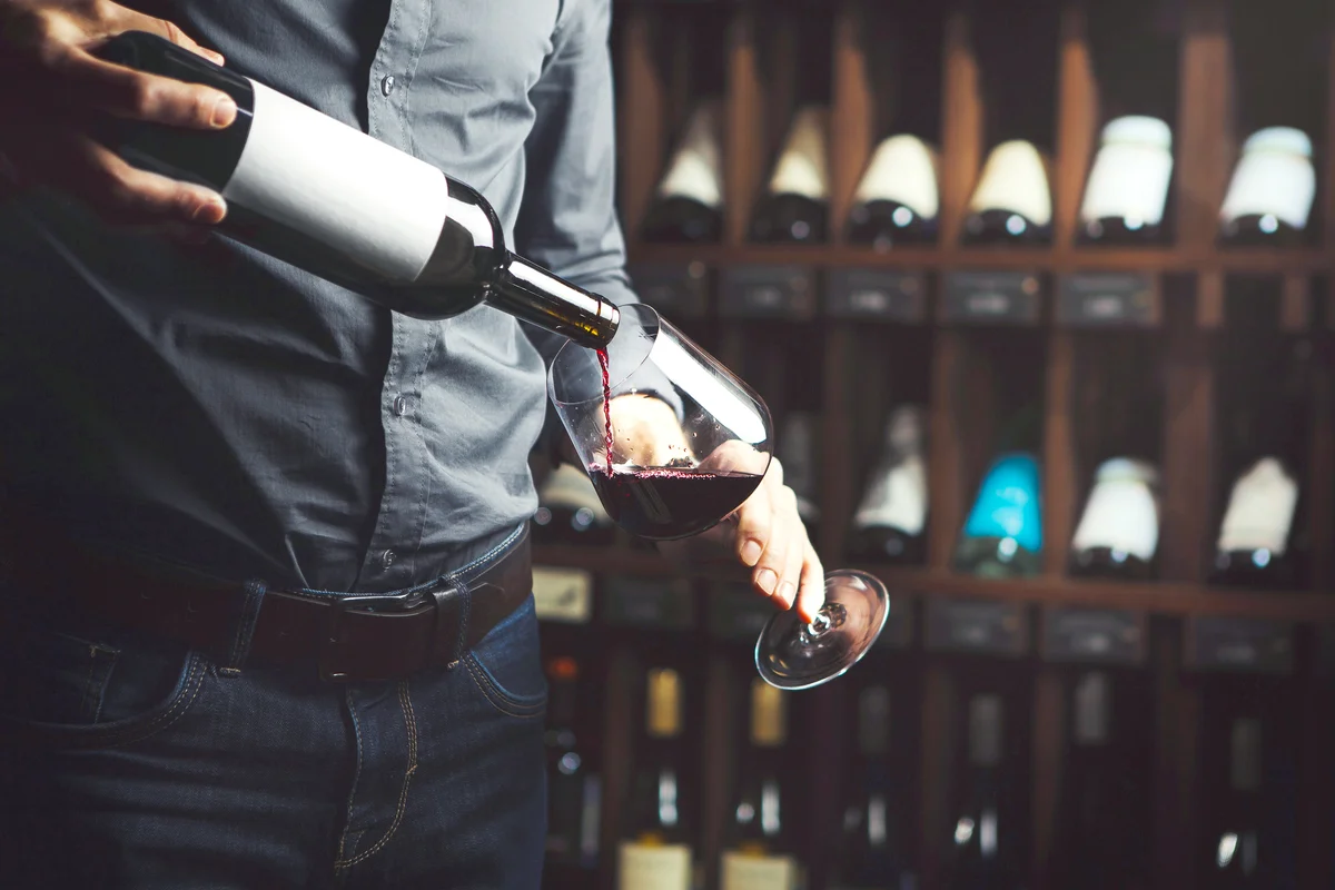 Sommelier pouring red wine from bottle in glass