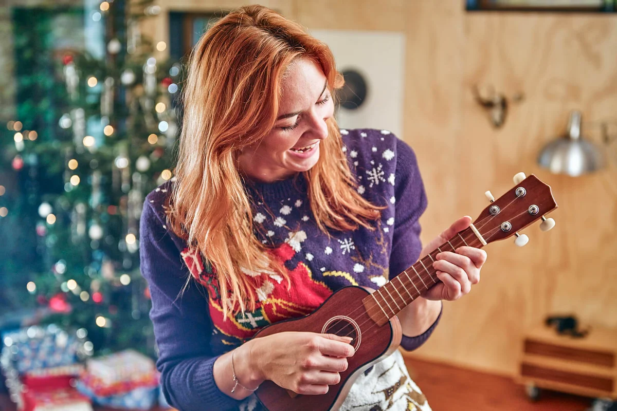 woman playing ukulele in front of Christmas tree