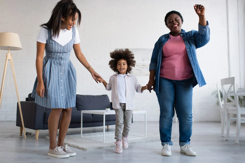 Cheerful African American girl with her mother and granny dancing together in the living room