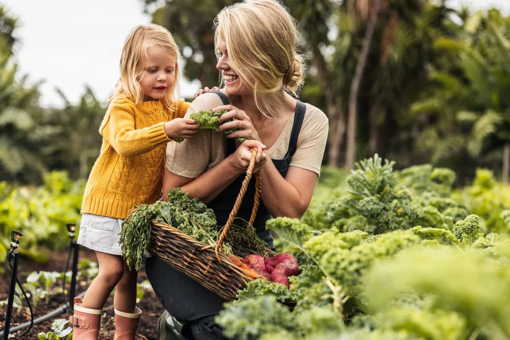 Happy mother picking fresh vegetables with her daughter in their garden