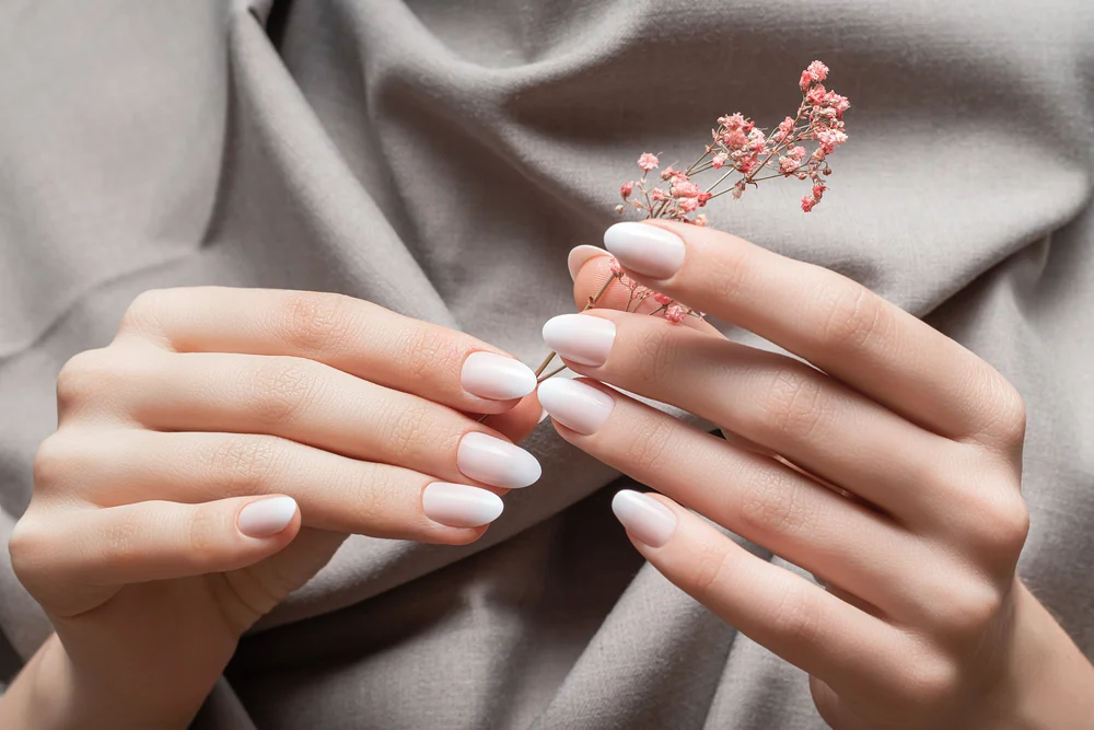 Female hands with a beautiful manicure holding a flower on a taupe fabric background.