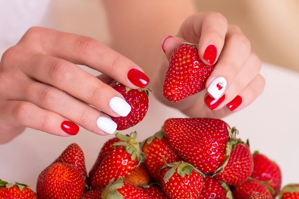 Female hands with a red and white manicure holding fresh strawberries