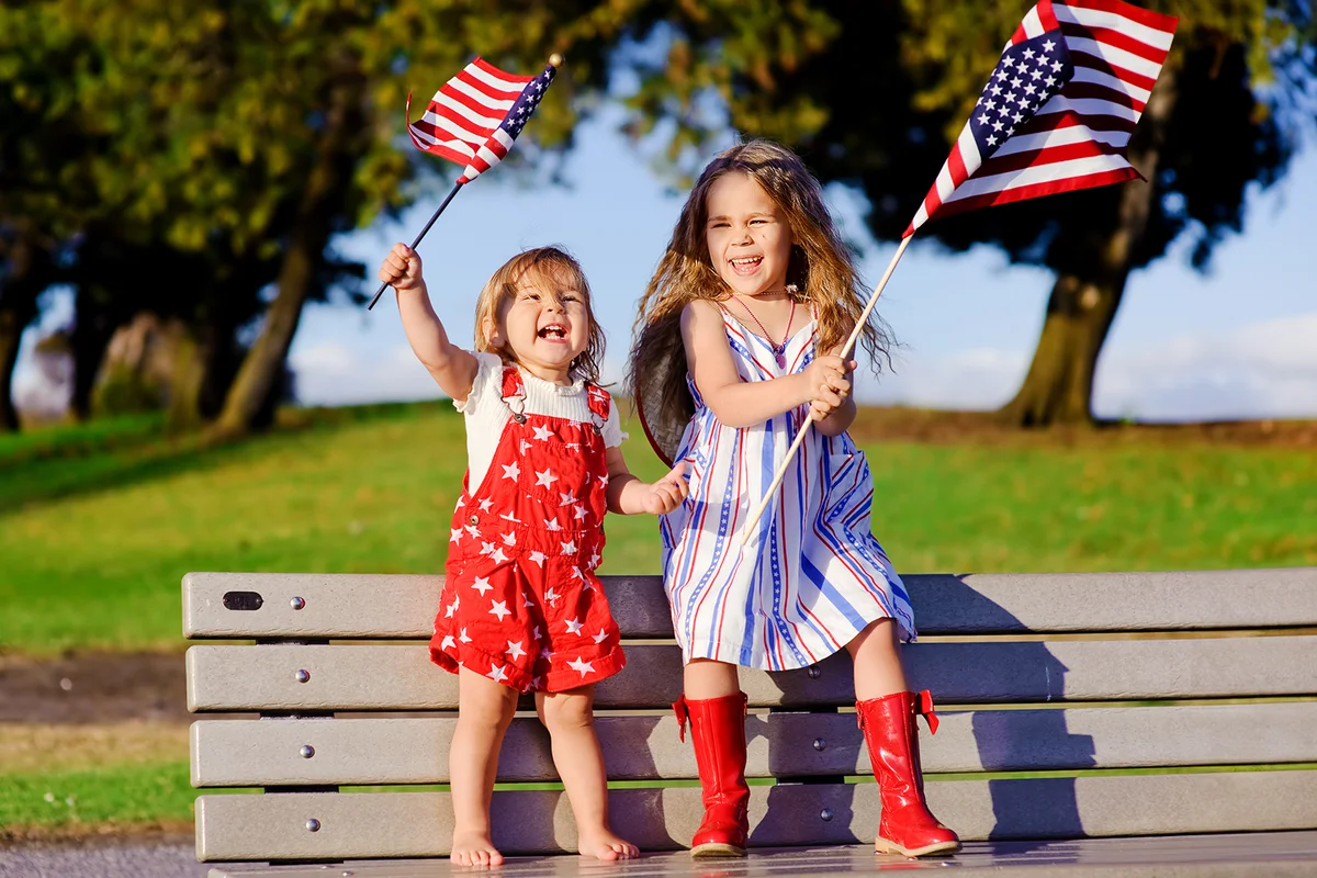 group of two happy adorable little kid girls smiling and waving American flag outside