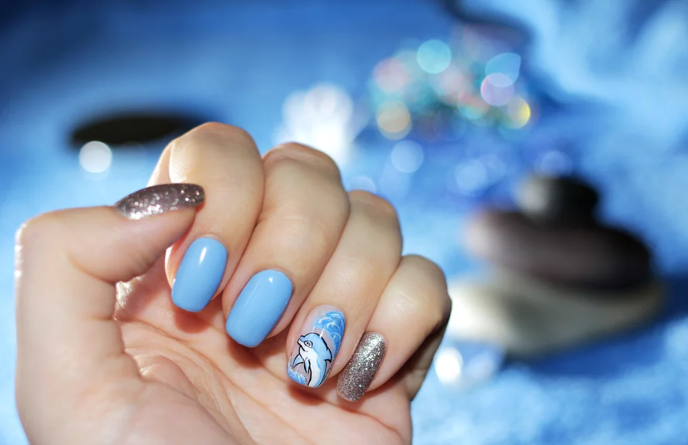 Close-up of hand with blue and white glittery nails and a dolphin design.