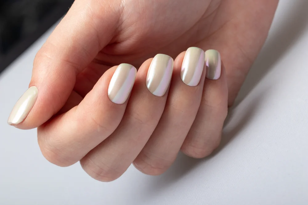 Close-up of a hand with short squared white pearl nails on a white background