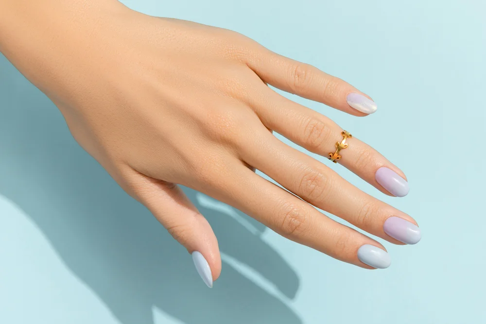 Top view of a female hand with a gradient blue and lavender manicure on a light blue background