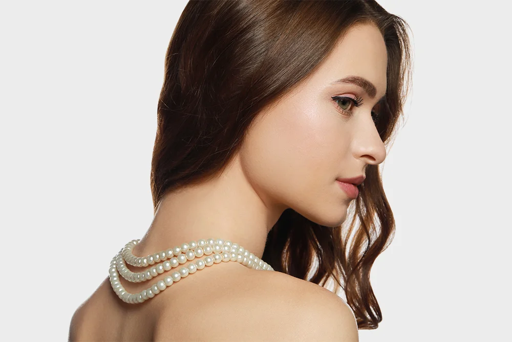 Close profile of a young woman wearing a layered elegant pearl necklace