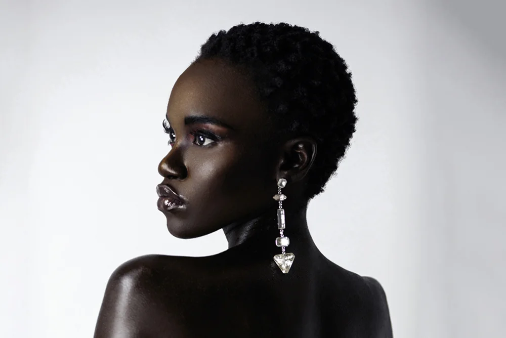 Portrait of a black woman with short black hair dangle earrings in front of a bright background