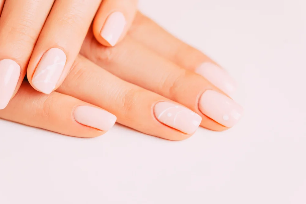 Closeup of female hands with a light pink manicure and an abstract design on a white background.