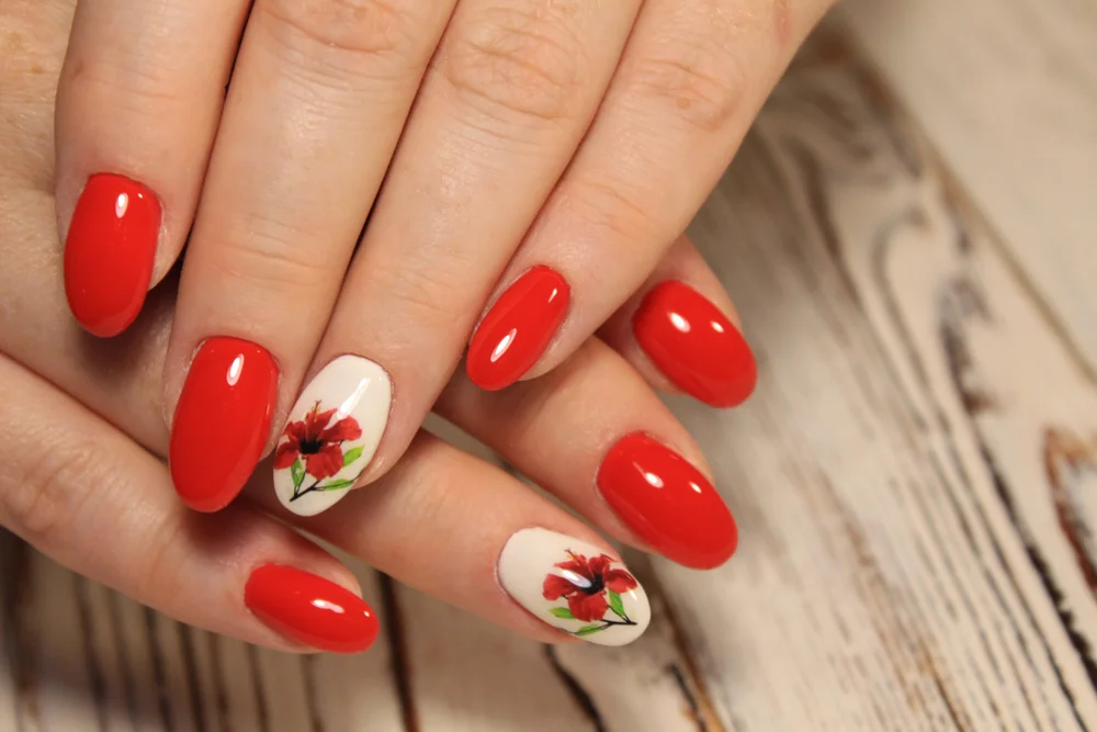 Close-up of a poppy red and beige manicure with the design of a flower on one of the nails