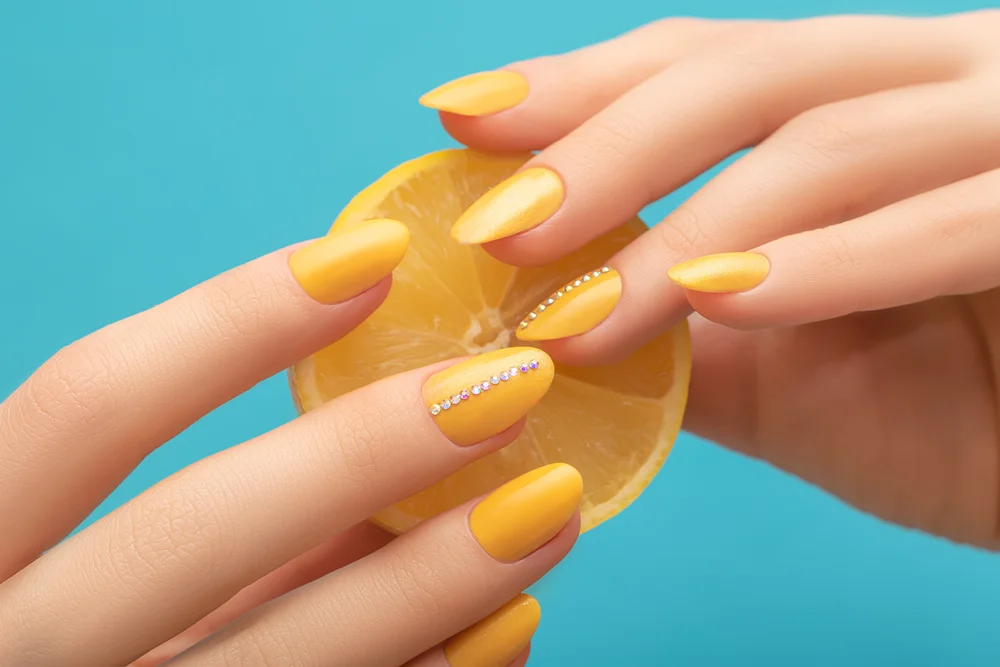 Female hands holding a half lemon with a yellow manicure on a blue background