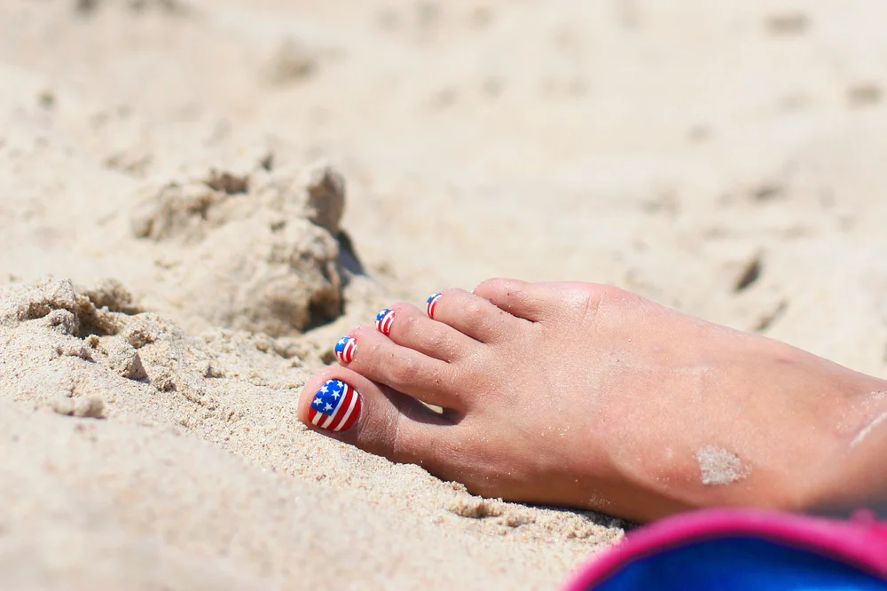 Pedicure in the sand with a US flag design on each nail