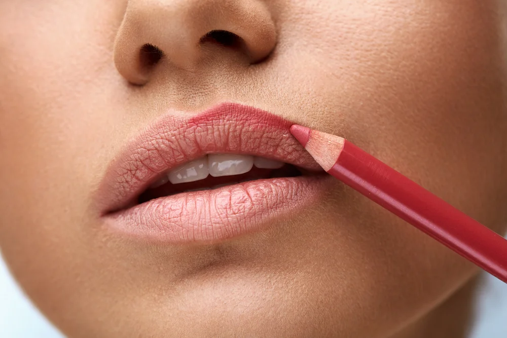 Close-up of a young woman applying red lip liner to her upper lip