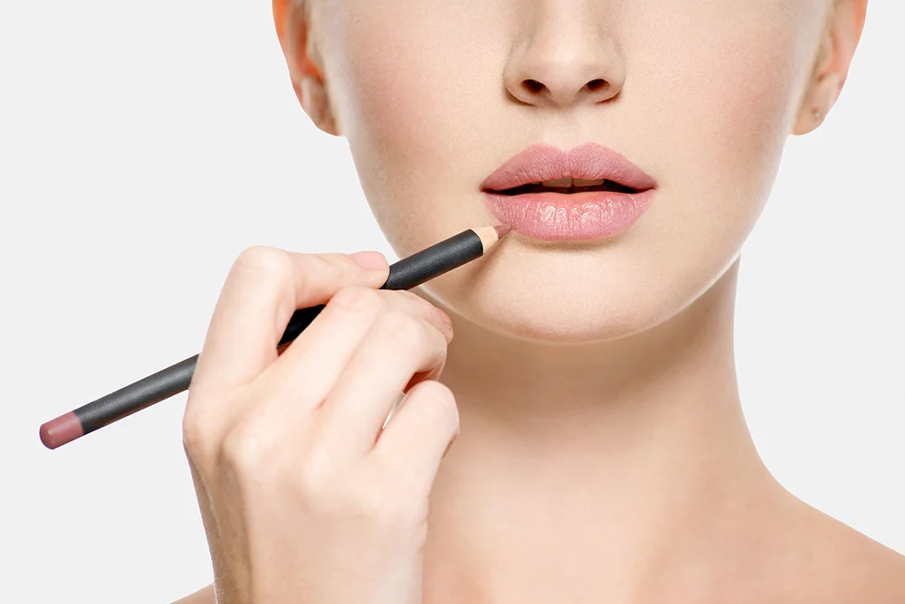 Woman applying liner pencil on her lips with a light grey background