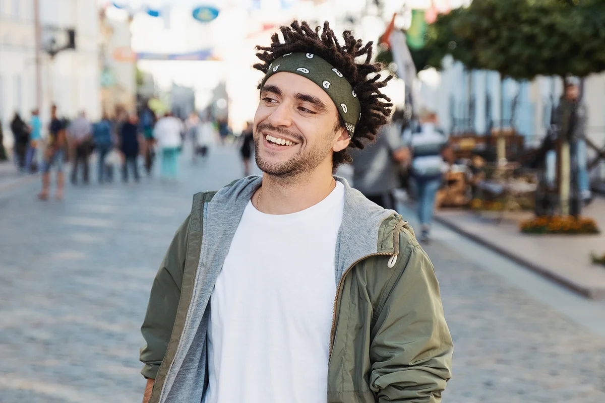 Young handsome beard man dressed stylish casual clothes, white t-shirt, green jacket, bandana posing outdoor