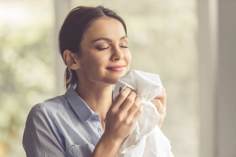 Close-up shot of woman smelling clean clothes and smiling while doing laundry at home