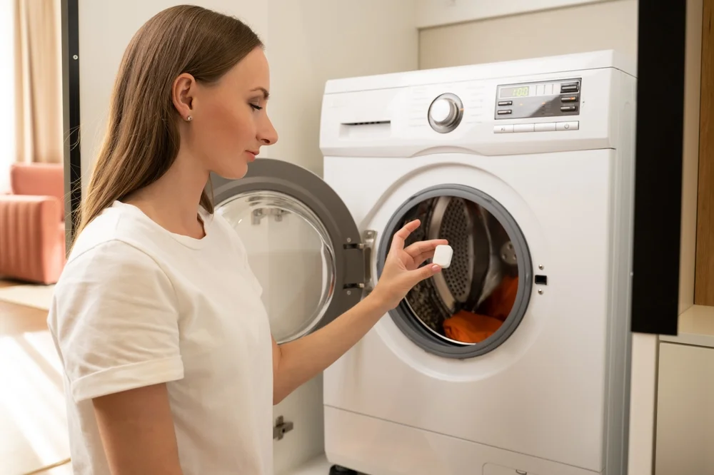 Woman puts a cleaning tablet in the washing machine.
