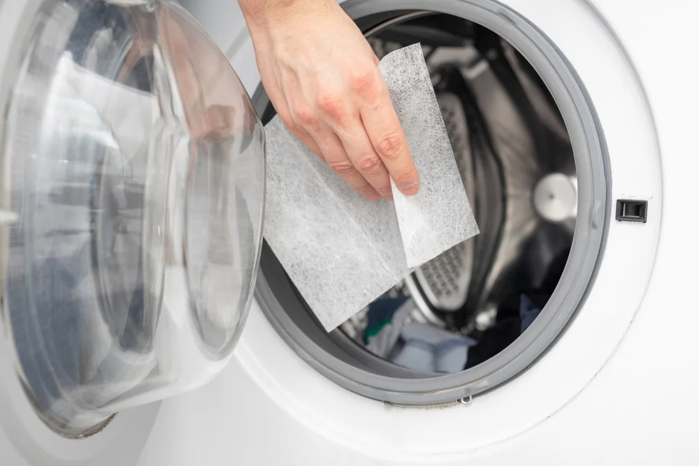 Man's hand putting a dryer sheet into the dryer