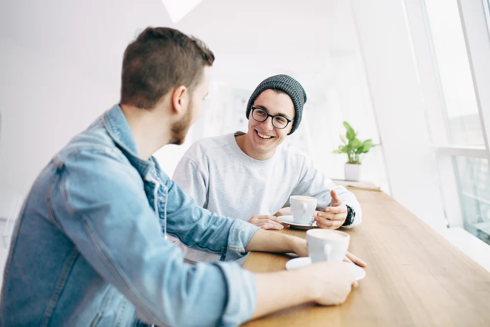 Two male friends laugh and talk over a coffee