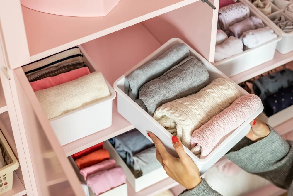 Close-up of woman's hands putting folded clothes in a container in the closet