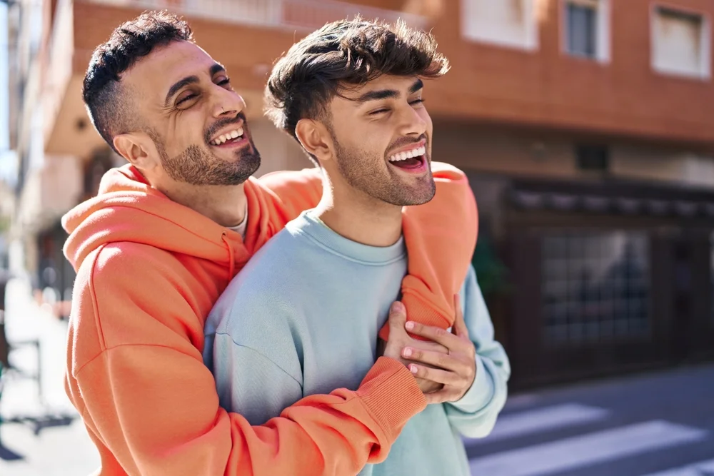 A happy couple of men hugging each other in the street on a sunny day