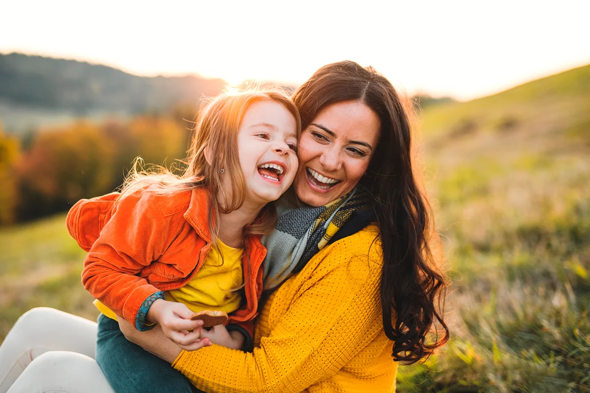 A portrait of young mother with a small daughter in autumn nature at sunset.