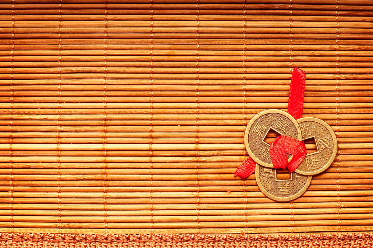 Three Chinese lucky coins tied with red ribbon on wooden mat