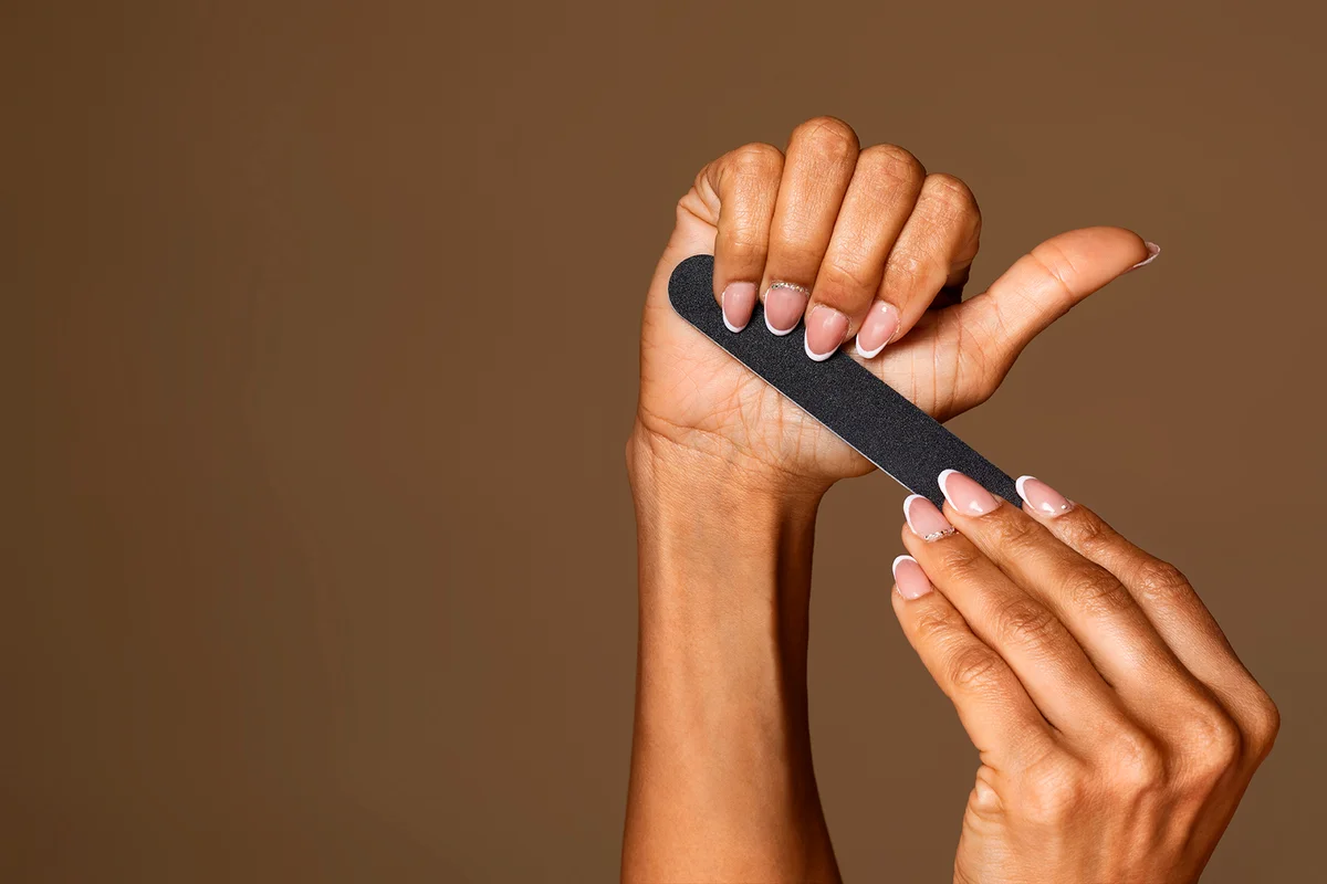 African american middle aged woman with manicure holding nail file isolated on brown studio background, free space, banner. Nail care concept