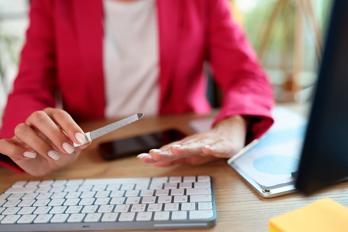 Business woman at workplace sawing nails with nail file. Nail care concept