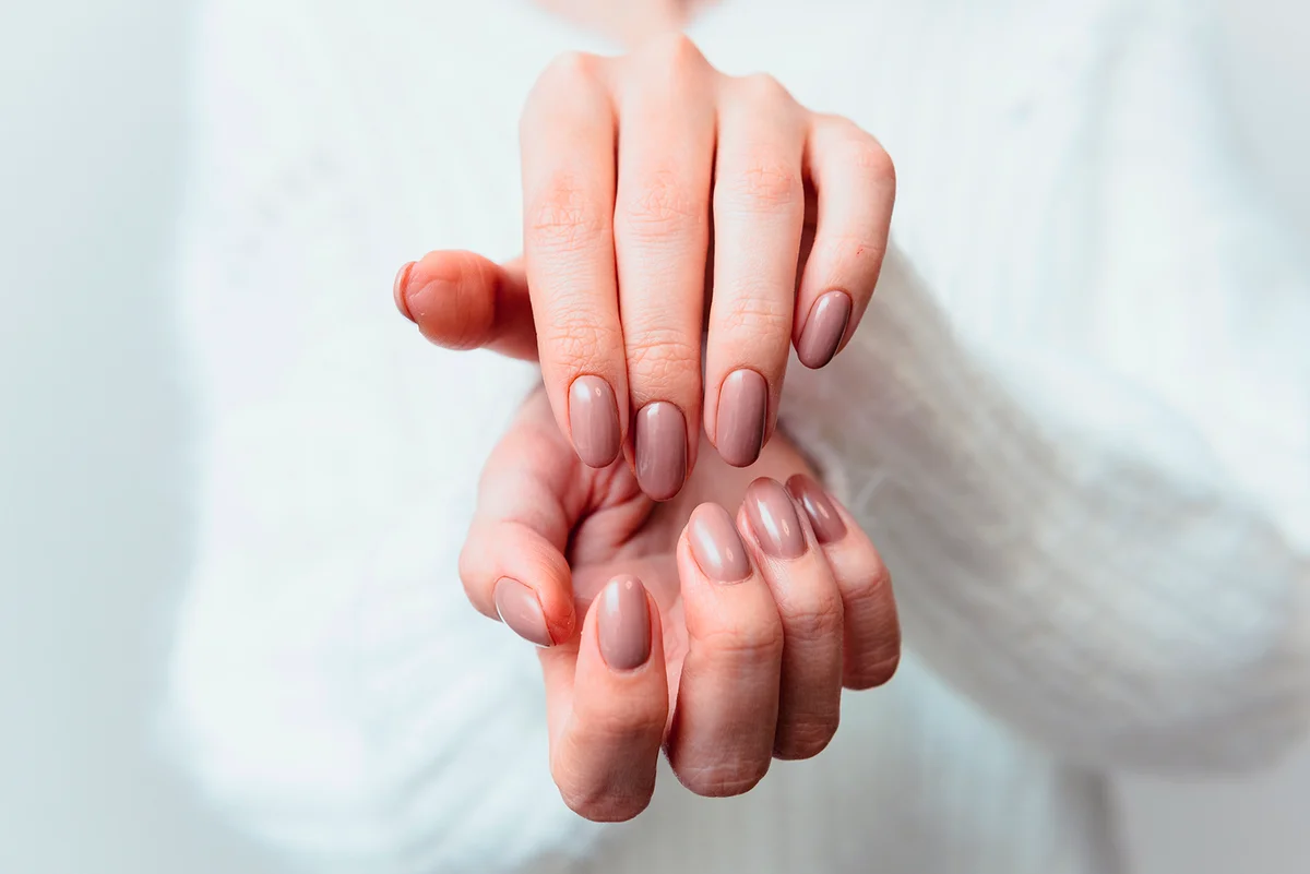 Beige manicure gel polish on beautiful oval nails of a woman in a white sweate.