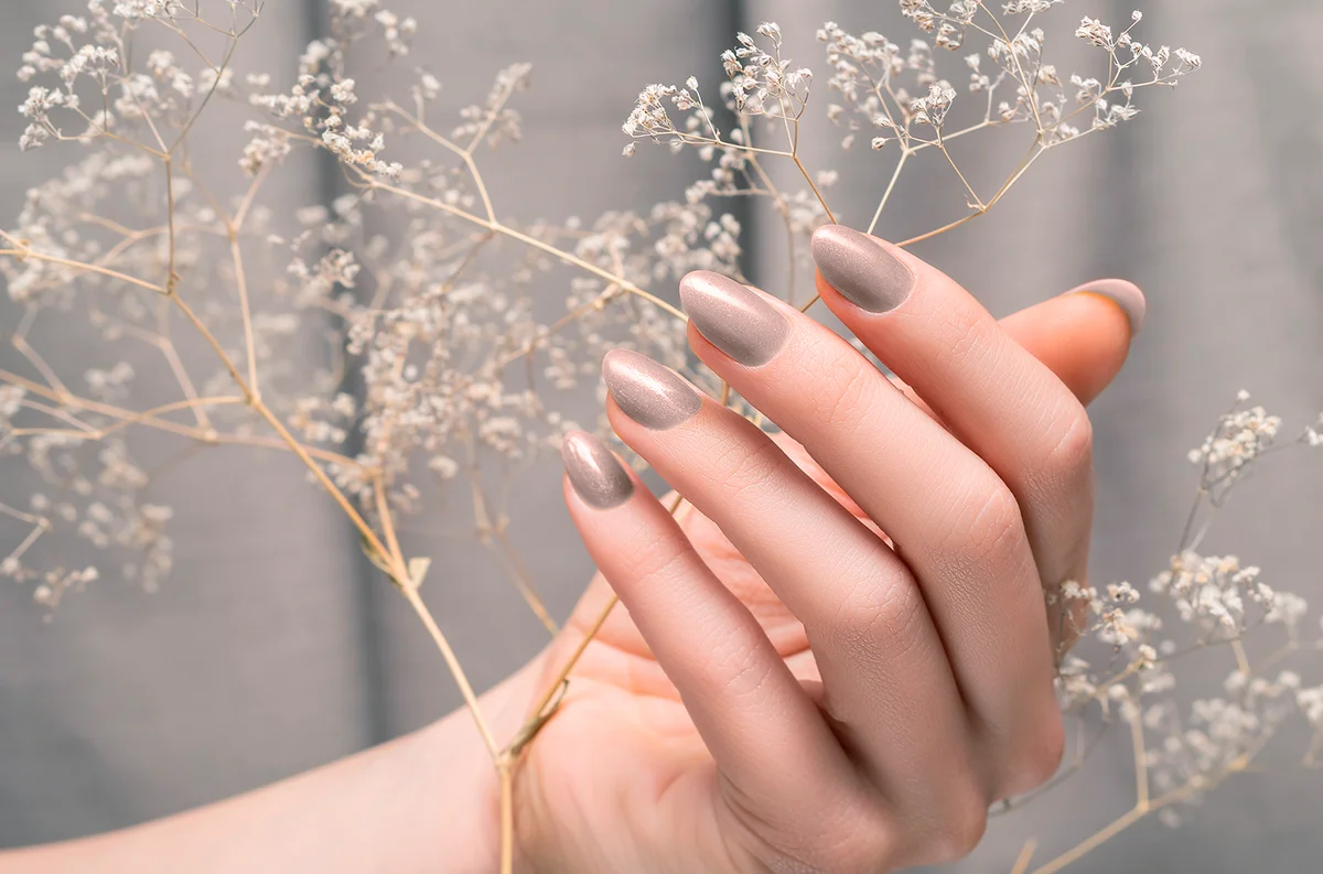 Female hand with glitter beige nail design. Female hand hold dry autumn flower. Woman hand on beige fabric background