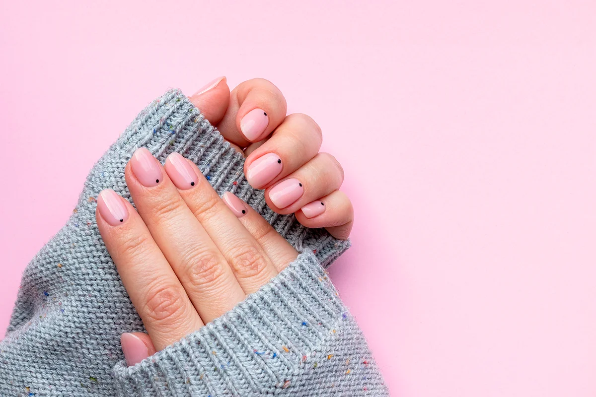 Female hands in a gray knitted sweater with trendy beautiful manicure - pink nude nails with black small