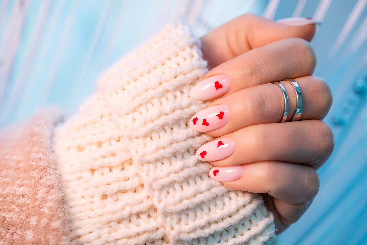Women's winter manicure with hearts for Valentine's Day. Well-groomed female hand with beautiful nails. Decorative gel polish in the salon.