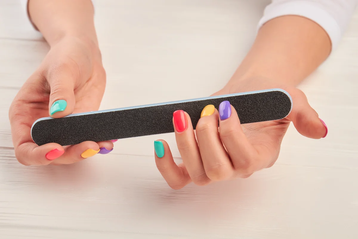 woman using nail file on colorful nails