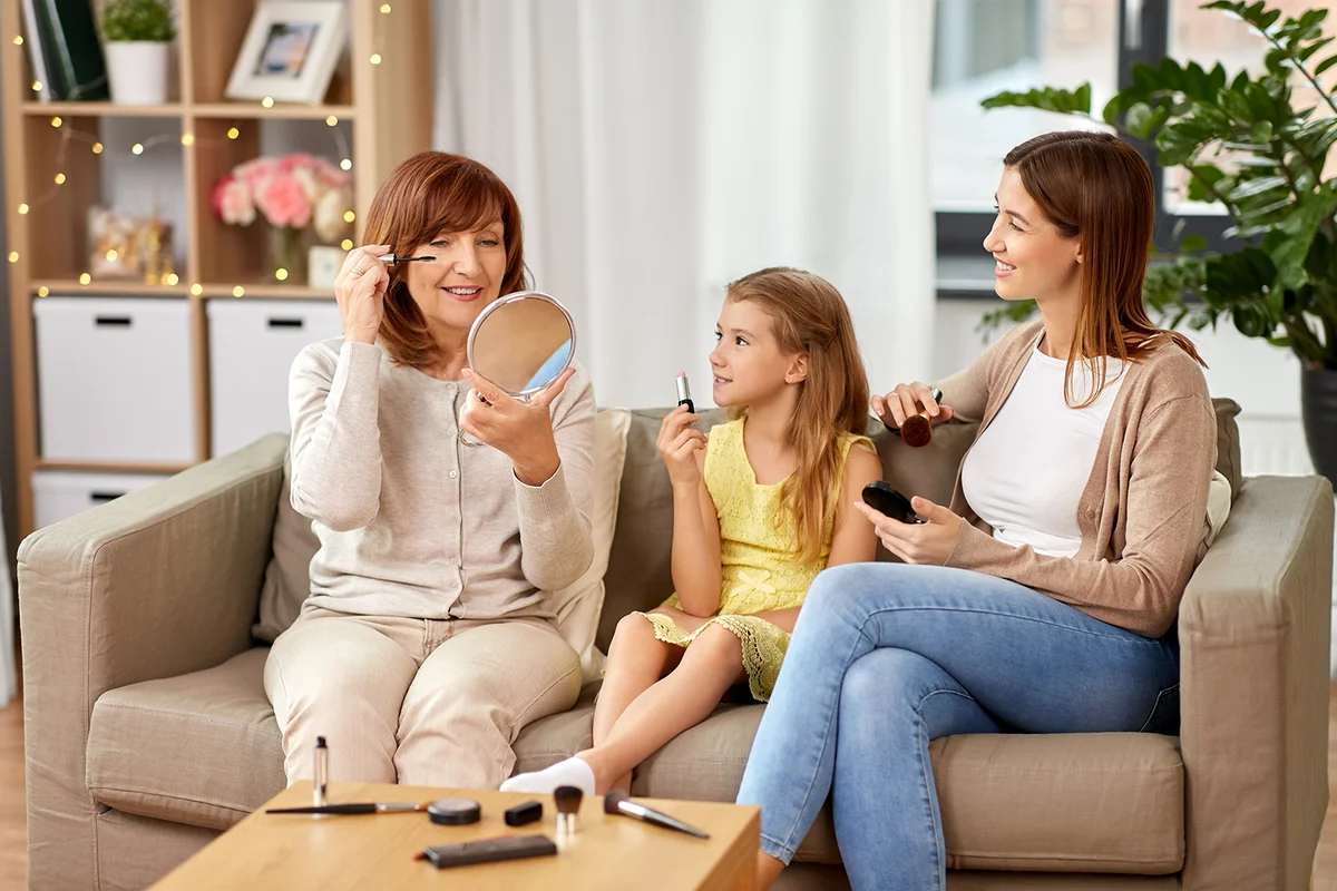 smiling mother, daughter and grandmother with cosmetics doing make up at home