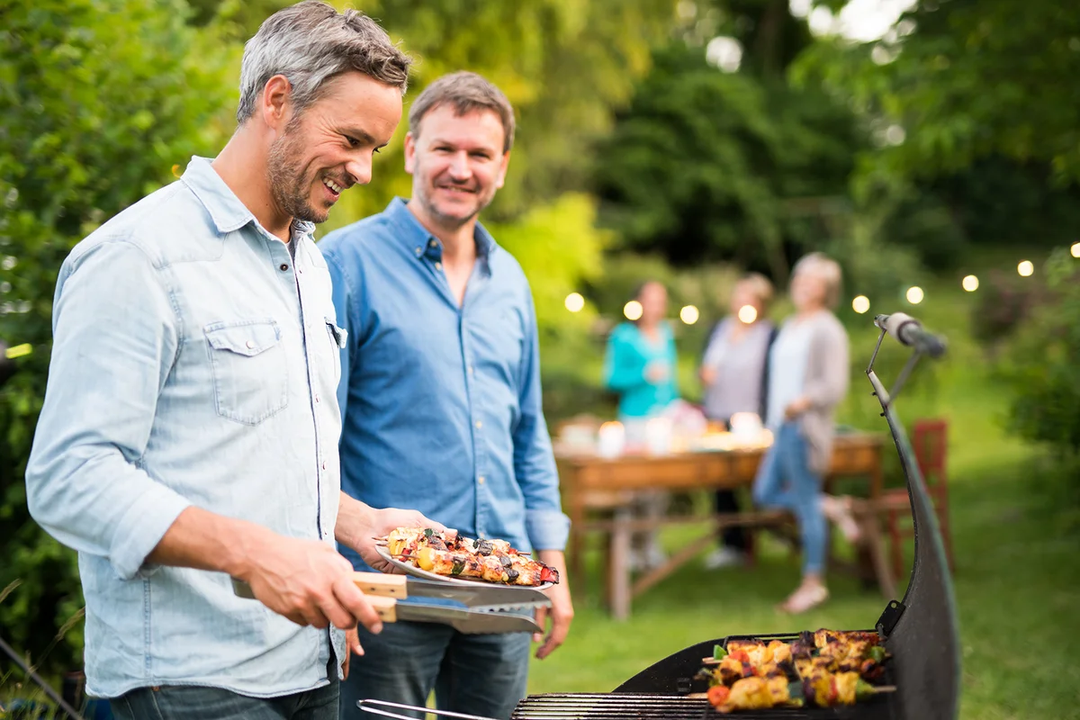 two men in their forties prepares a barbecue for friends