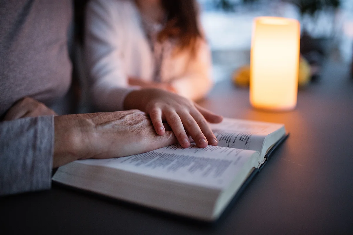 A small girl and grandmother reading bible at home