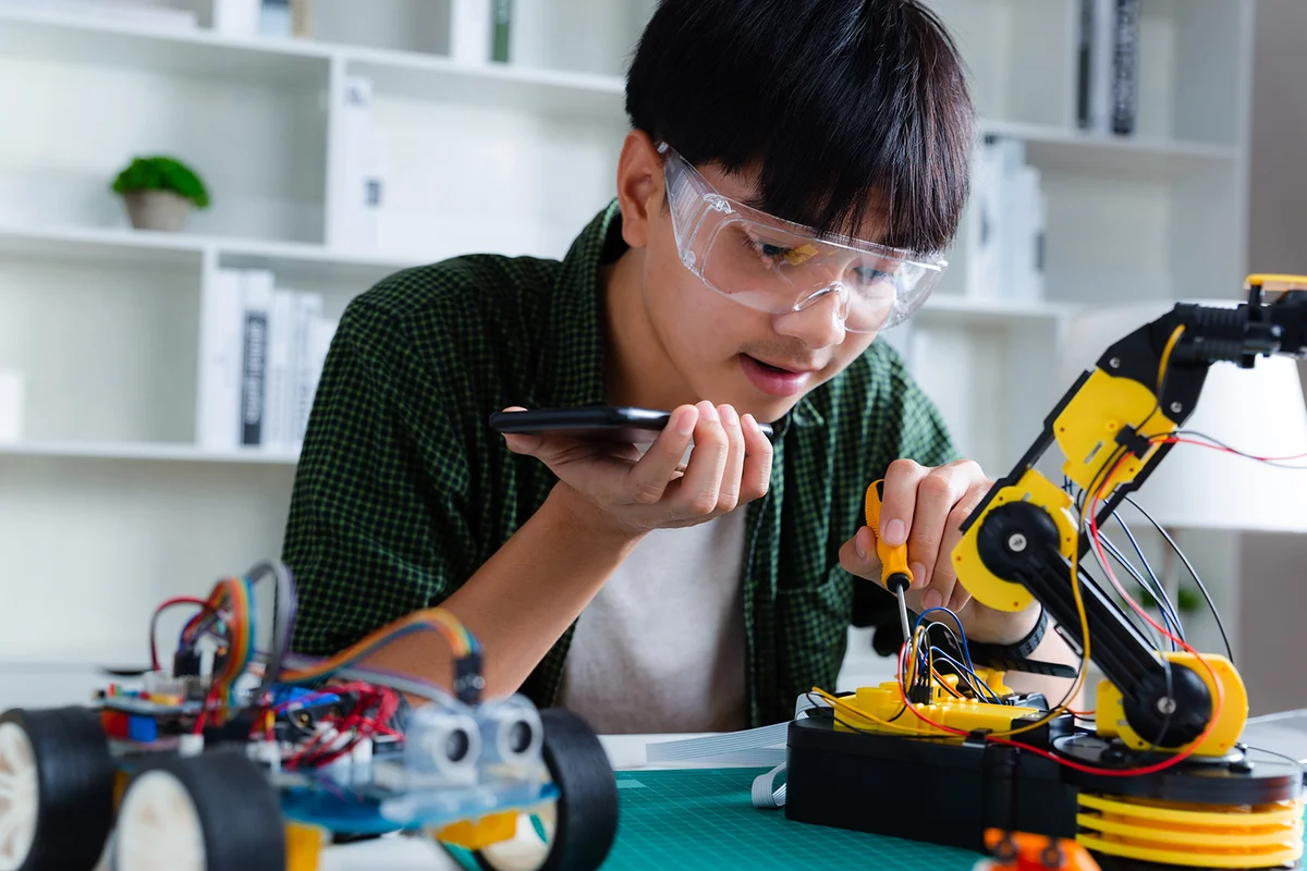 Teenager talks on smartphone with teacher about doing robots arm in house