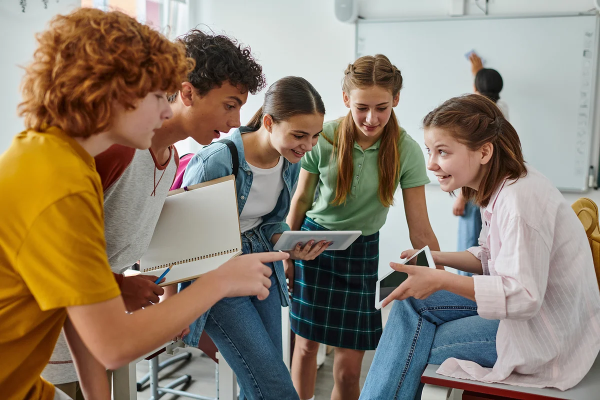 Smiling teen pupils using digital tablet together in classroom