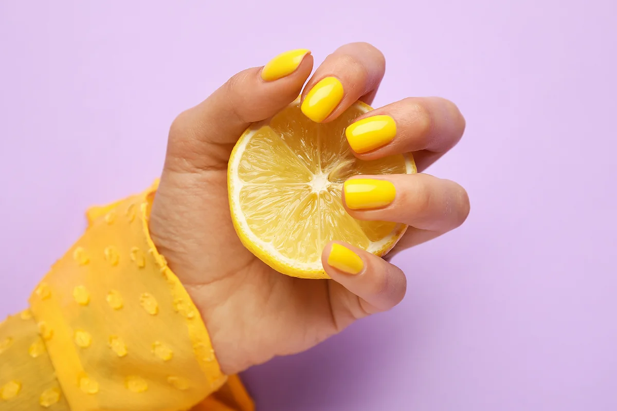 Woman with trendy manicure holding sliced lemon