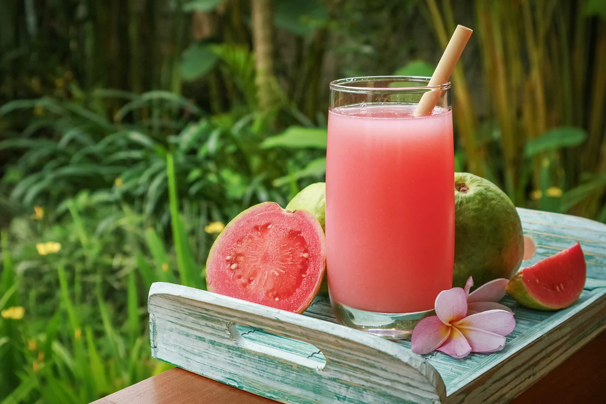 Guava mocktail in glass with bamboo drinking straw and fresh guava on tray outdoor