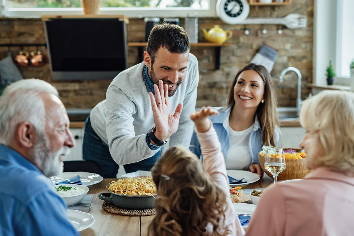 Happy father and daughter giving high-five to each other during a family lunch in dining room.