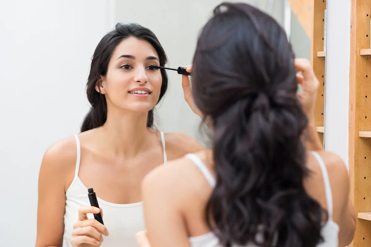 Woman applying mascara on eyelashes with makeup brush.