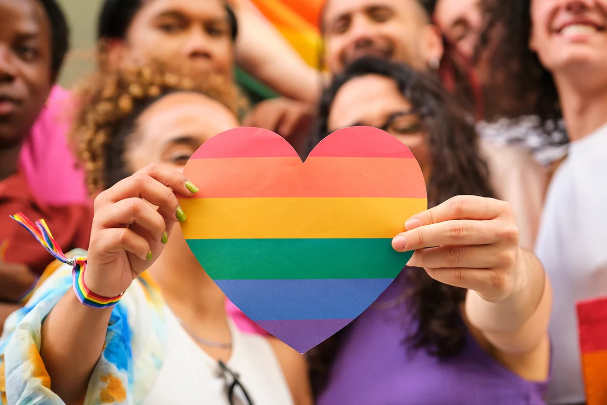 A group of LGBTQ people holding a rainbow heart celebrating International Pride Month
