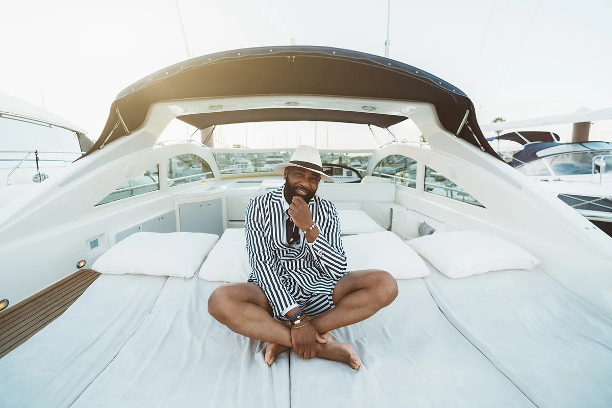 A cheerful wealthy guy sitting outdoors on the deck of a luxury yacht