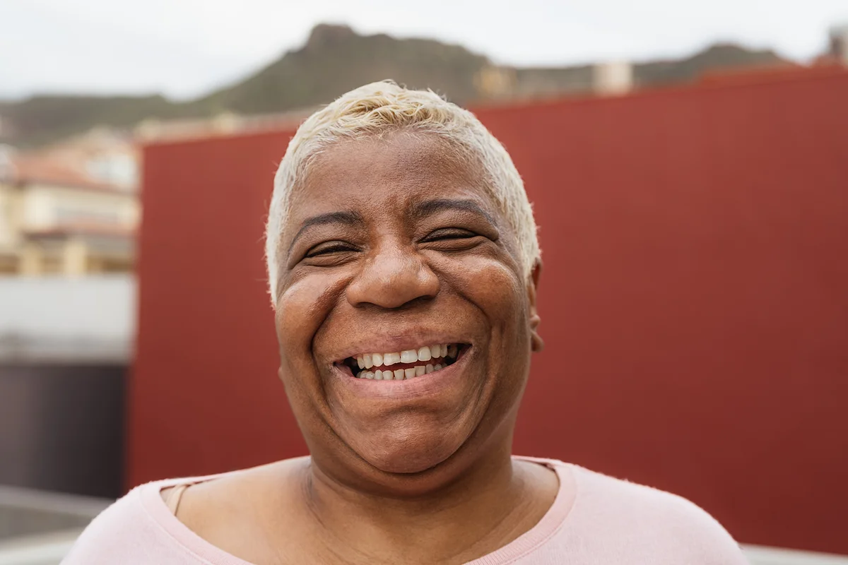 Happy Latin senior woman having fun smiling in front of camera on her house patio