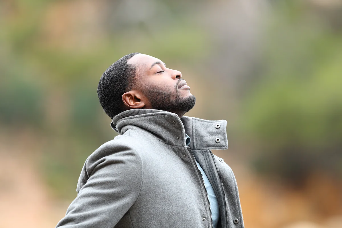 Relaxed man with black skin in winter breathing fresh air outdoors