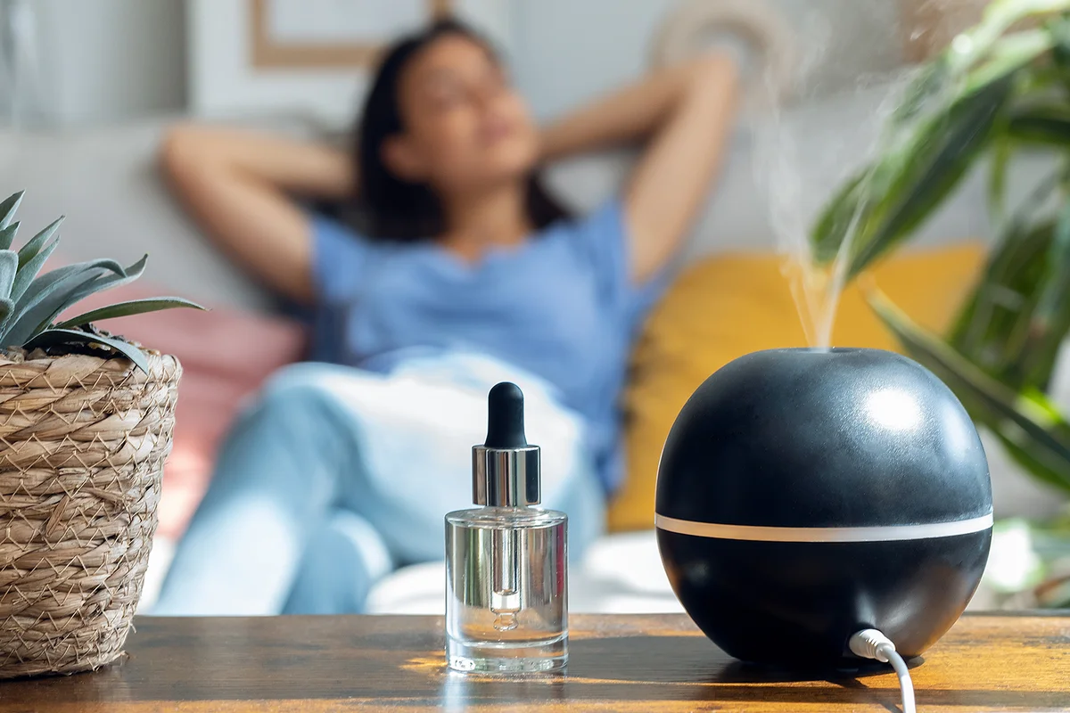 Shot of beautiful woman relaxing on a coach while essential oil aroma diffuser humidifier the air in living room at home