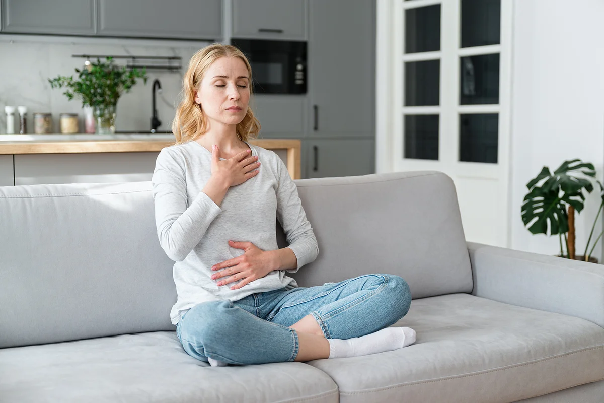Mindful young woman with hands on chest and stomach breathing out with closed eyes