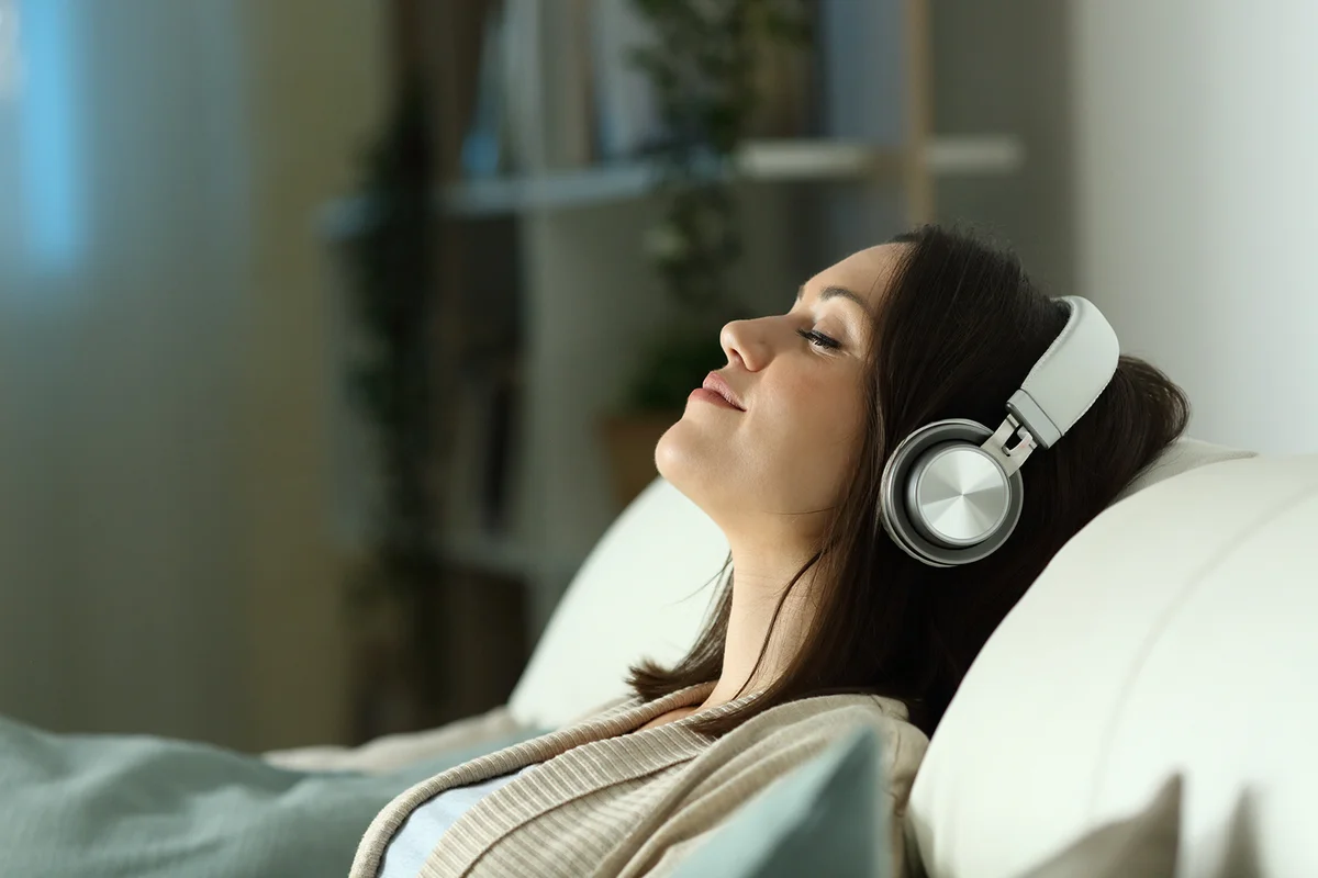Profile of a relaxed woman listening to music with headphones in the night sitting on a couch in the living room at home